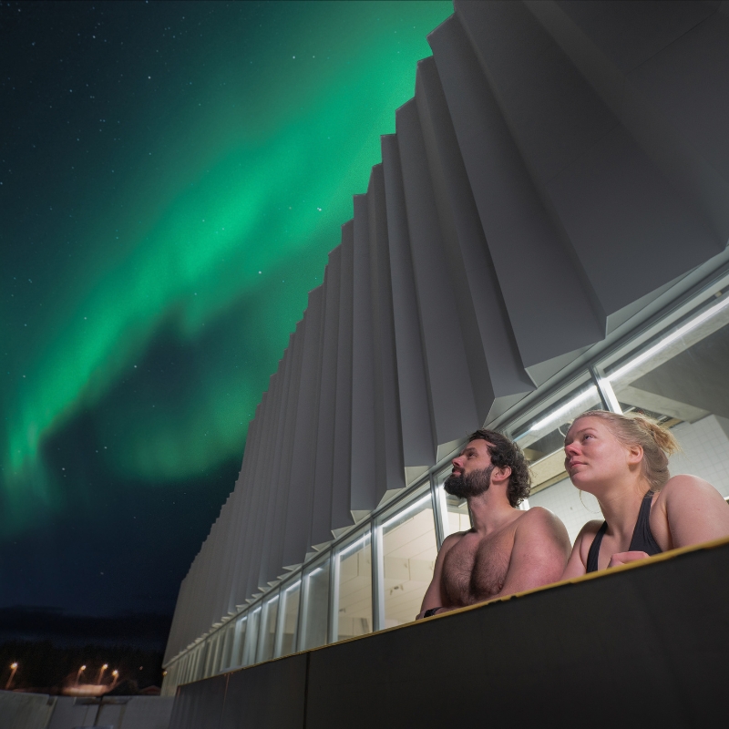 En person i Tromsøbadets utebasseng med nordlys over kveldshimmelen.