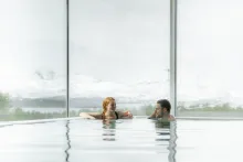 Two guests relaxing in an indoor pool at Tromsøbadet, with snow-covered mountains beyond the windows.